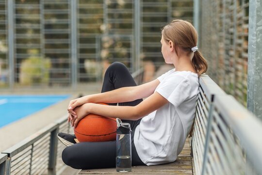 Basketball player resting alone outdoors with ball and water bottle