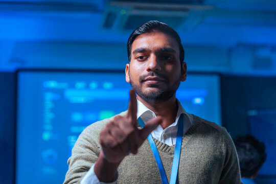 Confident Indian IT professional or developer touching a virtual screen in a modern tech office environment