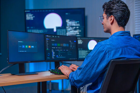 Male programmer working on software development with multiple computer screens in office