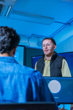Professional software engineer explaining data analysis to colleague during a late night working session in modern office with blue neon lighting