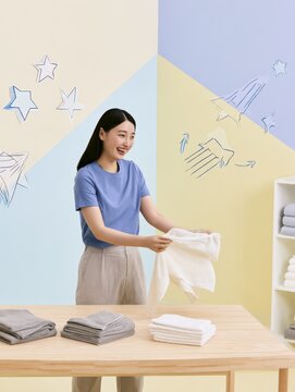 Happy young woman folding clean laundry on a wooden table in a bright room