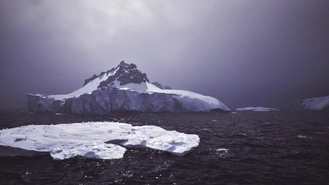 Antarctic iceberg and dark ocean, muted dawn light over jagged peak and frozen foreground, lonely atmosphere with distant swell research vessel beacon imagined
