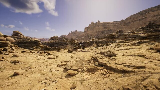 Sunlit rocky desert with sandstone ridges, expansive arid plain dotted with jagged outcrops and layered cliffs under clear blue sky warm ochre tones, deep
