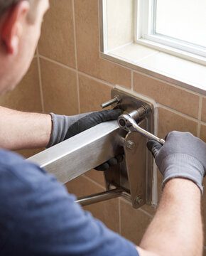 Contractor uses a socket wrench to tighten a shower safety seat bracket bolt on a tiled shower wall