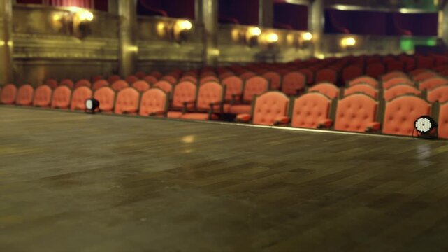 Bare stage after rehearsal, empty auditorium bathed in dim house light, lingering echoes and faint reflections on wooden floor, empty red rows and gilded