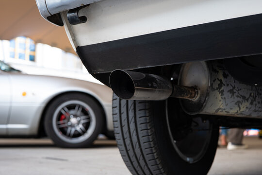 Low angle close up of single exhaust tailpipe and rear tire on a white classic car.