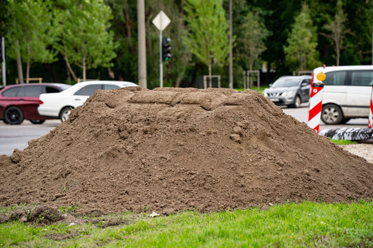 Excavated earth stockpile on a roadside verge beside temporary traffic markers, illustrating material handling and groundworks within an active road construction area