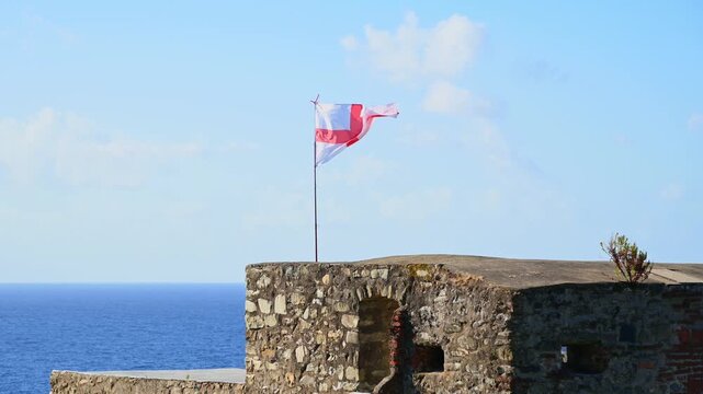 Genoese flag waving over coastal stone fort by open sea