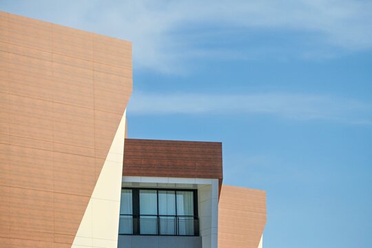 Modern architectural design featuring angular shapes and a large window against a clear blue sky.