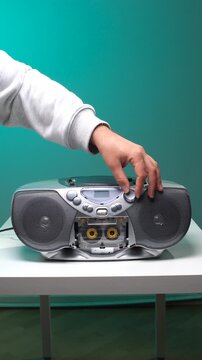 Vertical video human hand adjusting the volume dial on a vintage boombox with a transparent cassette tape playing inside, creating a nostalgic feeling of old school audio technology and music playback