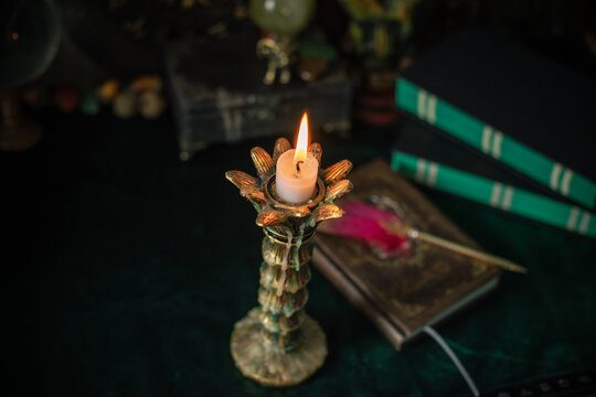 Burning candle in vintage candlestick on mystical altar with crystal ball, zodiac wheel, old spell books and dip pen 