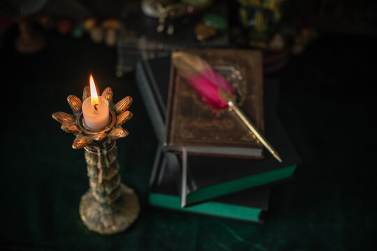 Burning candle in vintage candlestick on mystical altar with crystal ball, zodiac wheel, old spell books and dip pen 
