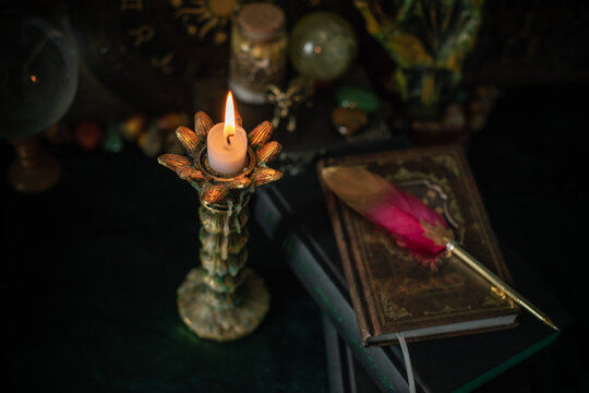 Burning candle in vintage candlestick on mystical altar with crystal ball, zodiac wheel, old spell books and dip pen 
