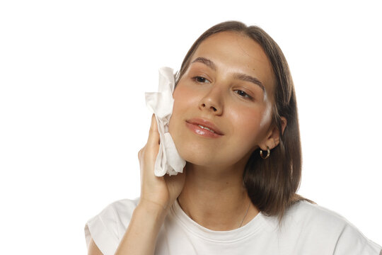 Portrait of a young woman wiping her face with wet wipes, skincare routine, on white background.