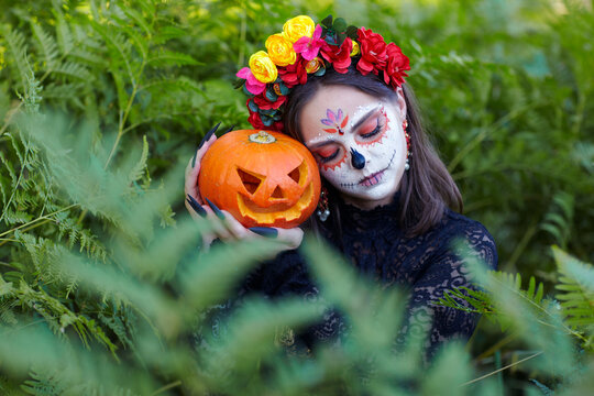Halloween beauty portrait of female sleeping among ferns with Halloween pumpkin in hand. Eyes closed