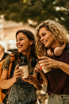 Young women friends walking city enjoying coffee