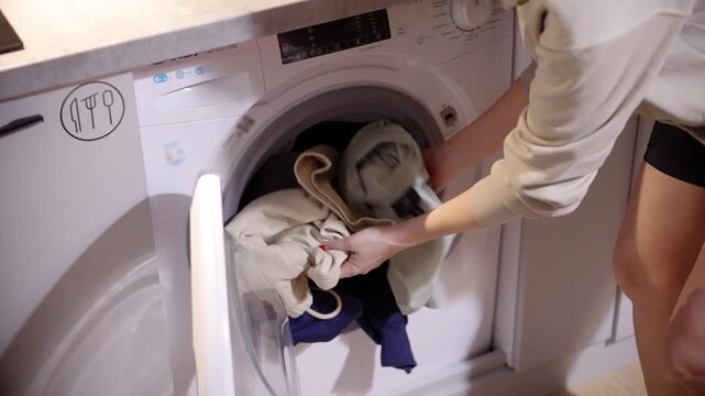 Person Loading Dirty Clothes Into Washing Machine Drum. Laundry Appliance Operation. Clothes Care 