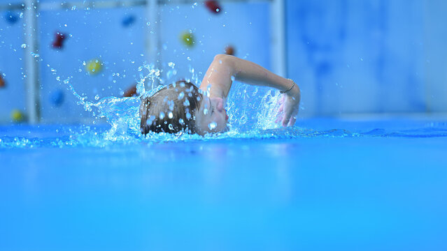 Child swimming freestyle stroke creating water splash