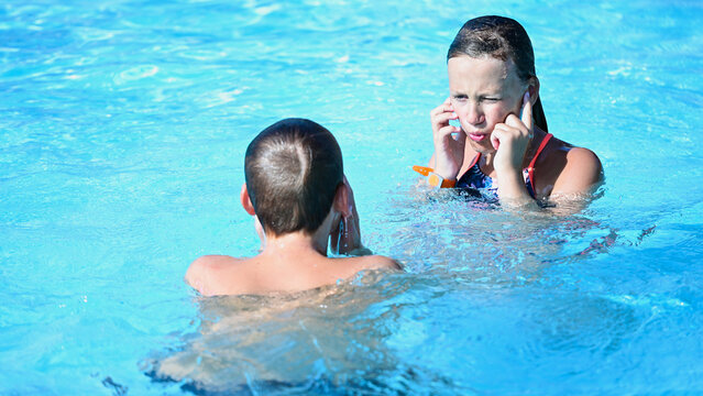 Two children covering ears from loud noise while swimming in a pool during summer