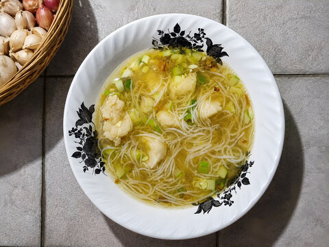 Traditional Palembang tekwan soup from Indonesia, featuring delicate fish dumplings, rice vermicelli, chopped spring onions and golden clear broth with aromatic oil, photographed from above on a bowl.
