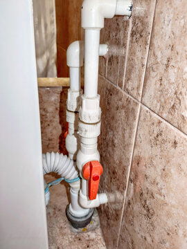 White old plastic water pipes with red shutoff valve installed in bathroom. Plumbing supply lines and drainage system connections