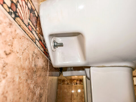 Wall mounted washbasin installation with metal bolt and washer. Detail of ceramic sink hardware attached to bathroom tiled wall