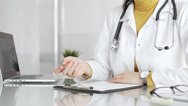 Doctor working on medical records, writing prescription in clinic office, using laptop for patient data management. Medicine, healthcare and science concept