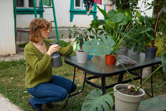 Woman spraying tropical houseplants in an outdoor garden