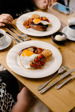 People eating breakfast of eggs, sausages, and beans in restaurant.