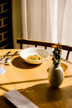 Minimalist table setting with pasta bowl in sunlit fine restaurant.