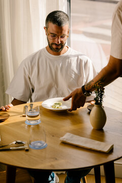 Waiter serving haute cuisine to man at sunlit minimalist table.