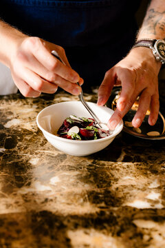 Chef's hands using tongs to plate salad in luxury restaurant.