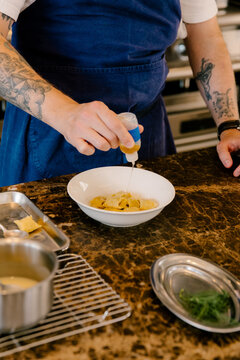 Chef using a dropper to drizzle seasoning over pasta in a restaurant