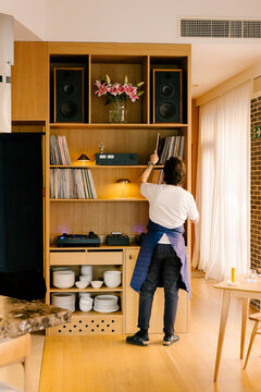 Wide shot of a chef browsing a vinyl record collection on a shelf