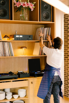 Full body shot of a man selecting a vinyl record from a bookshelf