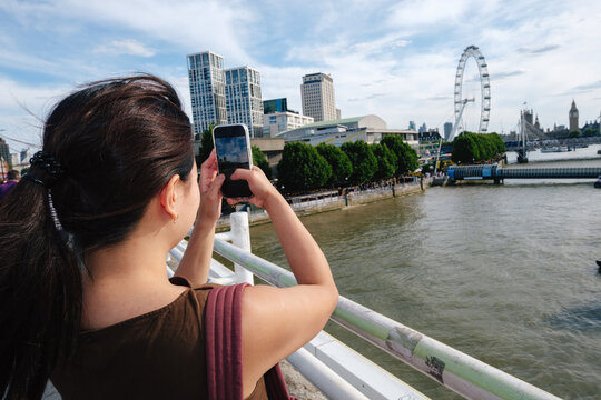 Tourist capturing London cityscape with smartphone on River Thames