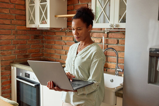 Woman stands in the kitchen, holding her laptop
