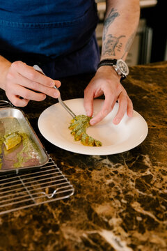Chef's hands using tongs to plate gourmet dish