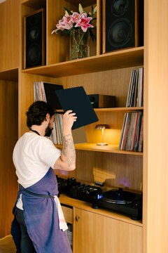 Wide shot of a chef picking up a vinyl record from a shelf
