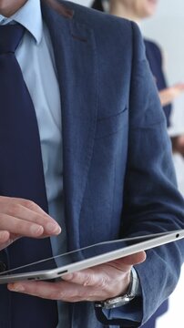 Businessman in a suit using a tablet during a corporate meeting, interacting with the touchscreen as blurred colleagues collaborate in the background, modern workplace tech