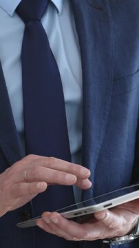 Businessman in a suit using a tablet during a corporate meeting, interacting with the touchscreen as blurred colleagues collaborate in the background, modern workplace tech