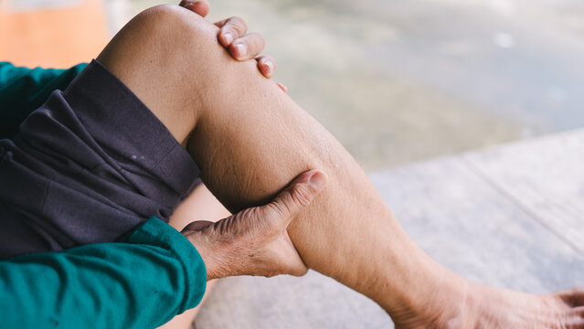 Detailed close-up of an elderly adult pressing their aching calf muscle outdoors. The senior is experiencing severe leg pain, poor blood circulation, and physical strain. Aging wellness concept.