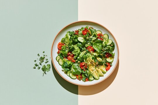 Vegan salad bowl with avocado, cucumber and tomato on a dual-tone surface, featuring fresh textures and copy space for nutrition campaigns