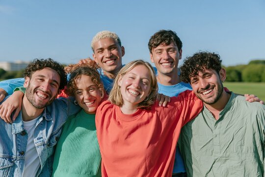 Group of six diverse young friends smiling and hugging in a sunny green park, natural and authentic, for youth community and friendship themes