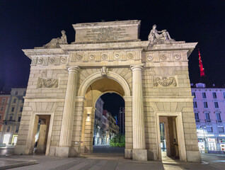 Fototapeta premium Porta Garibaldi glows against Milan's night sky, its neoclassical arches framing the illuminated street beyond - a timeless gateway honoring the city's revolutionary past.