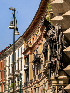 Ornate Italian facades curve beneath a bronze chimera perched against textured stone, blending classic architecture with striking sculptural detail in Milan Italy.