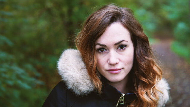 outdoor portrait of young woman wearing winter jacket with fake fur lined hood in forest