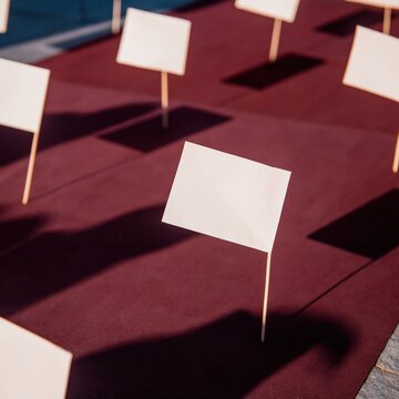 Plain paper flags on wooden dowels arranged in a repetitive pattern on a deep burgundy background for festive banners and holiday cards