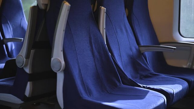 interior of a train with blue upholstered seats arranged in rows. Natural light filters through the windows, highlighting the fabric of the seats