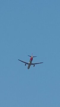Low angle shot of a commercial airliner flying across clear blue sky overhead, zooming out to show urban power lines, street light, and elevated concrete bridge structure.
